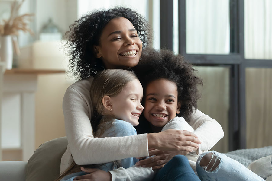 A young woman is seen hugging two young children and smiling because she volunteers in helping children in the foster care system in Springfield, IL.